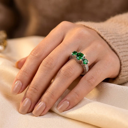 Anel prateado com três esmeraldas, joia elegante da marca Rose & Oliver, destacando as pedras verdes e o design refinado.